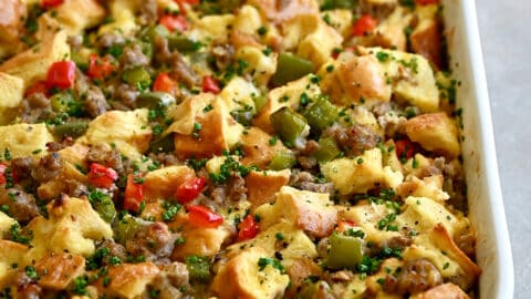 An egg casserole with breakfast sausage and colorful bell peppers in a white baking dish next to a bowl of fresh berries.