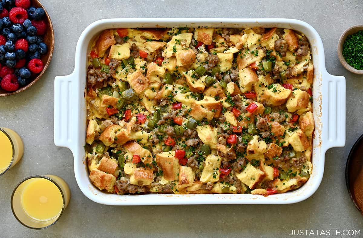 A top-down view of an egg casserole in a white baking dish next to two glasses containing orange juice.