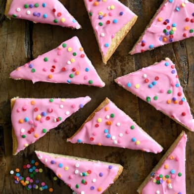 Pink-frosted sugar cookie bars with rainbow sprinkles next to a small bowl containing sprinkles.