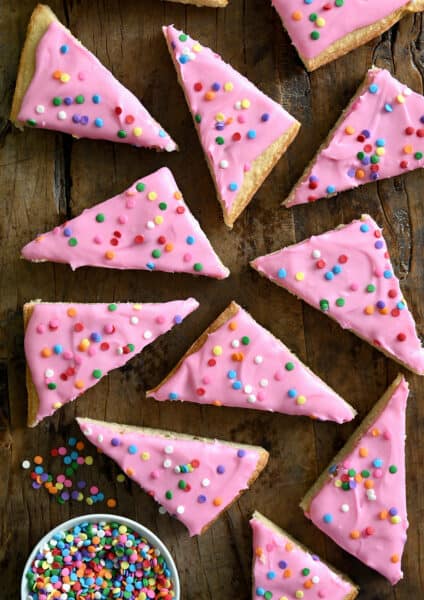 Pink-frosted sugar cookie bars with rainbow sprinkles next to a small bowl containing sprinkles.