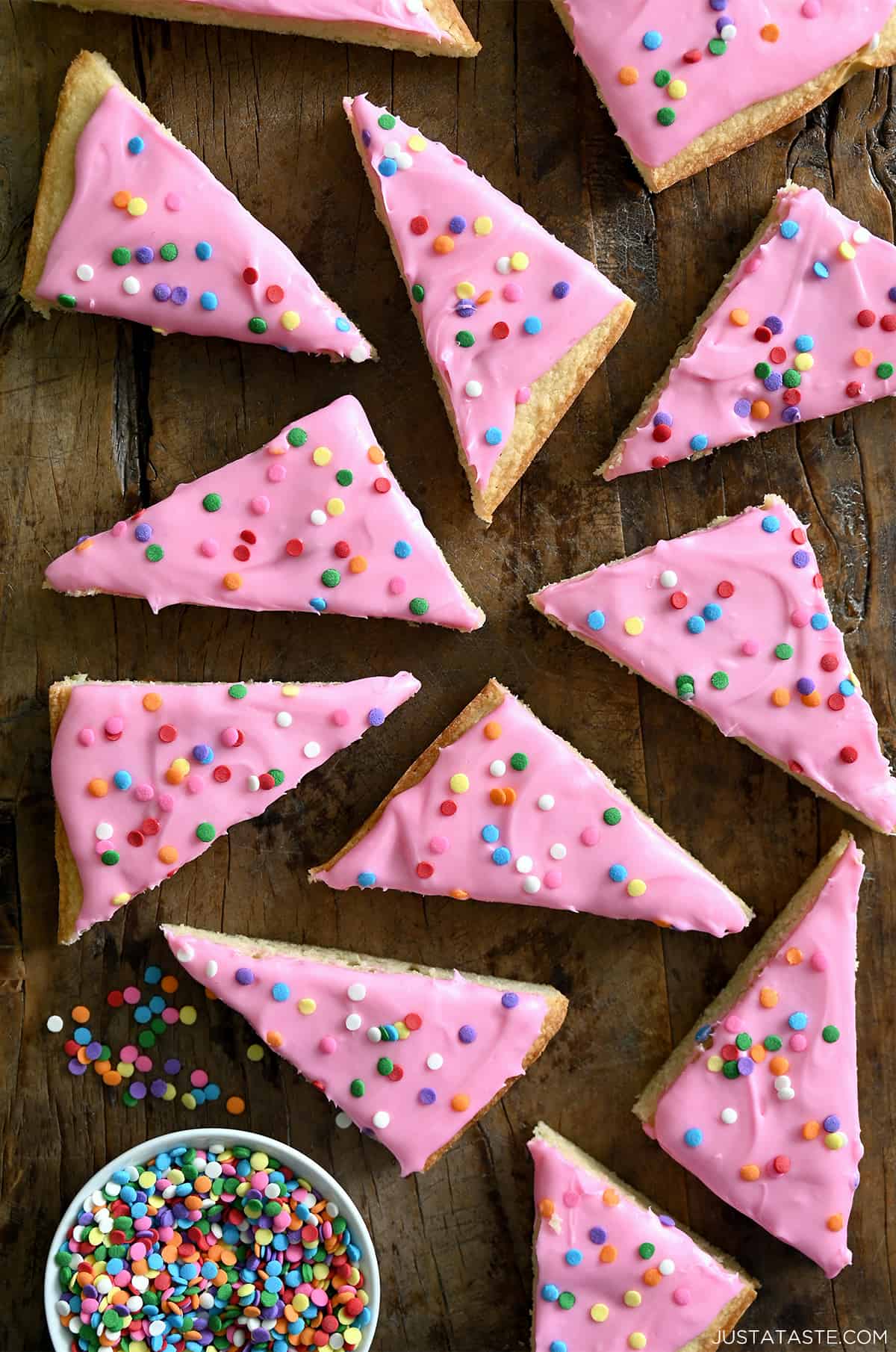 Pink-frosted sugar cookie bars with rainbow sprinkles next to a small bowl containing sprinkles.