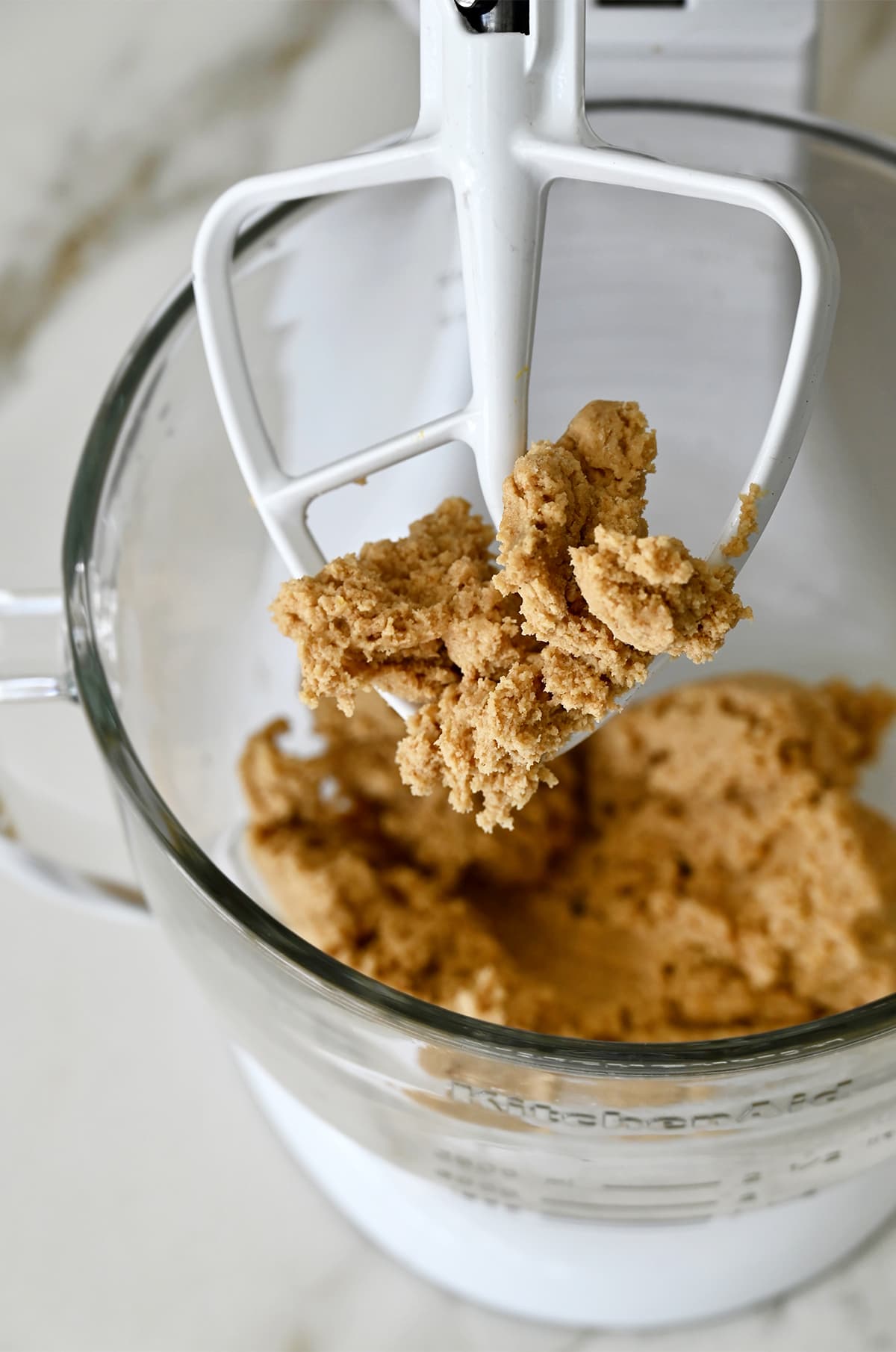 A stand mixer with a paddle attachment covered in graham cracker cookie dough.