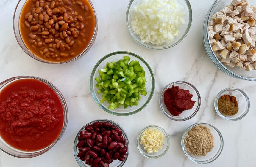 Various sizes of bowls containing diced onions, green bell pepper, beans and spices