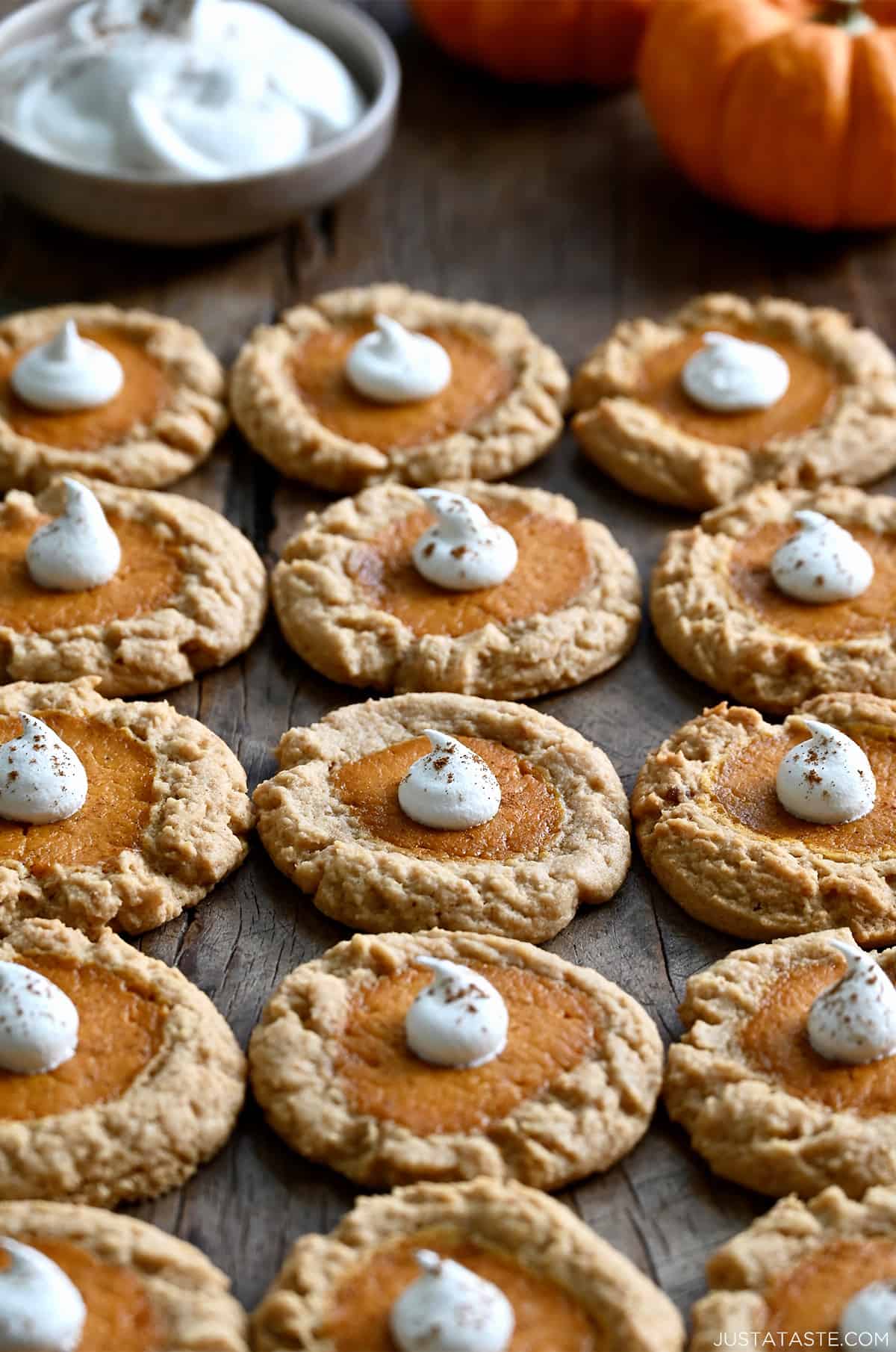 Rows of pumpkin cheesecake cookies all topped with a small dollop of whipped cream and sprinkled with pumpkin spice.