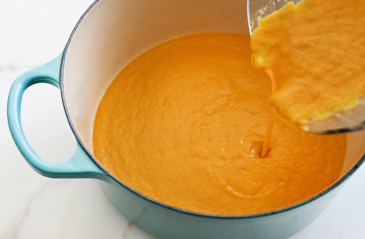 Pumpkin soup being poured from a blender into a large stockpot.