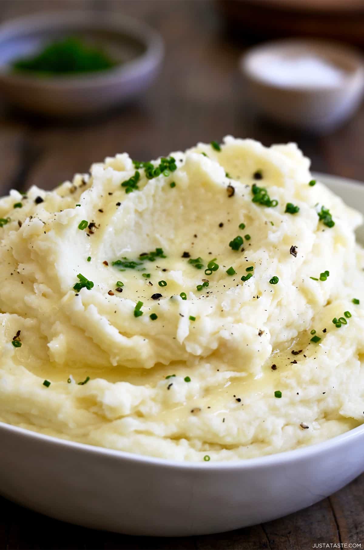 Creamy mashed potatoes topped with chives, black pepper and butter in a large serving bowl.