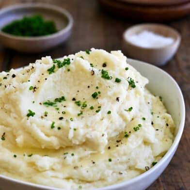 Creamy mashed potatoes topped with fresh chives and black pepper in a white serving bowl.