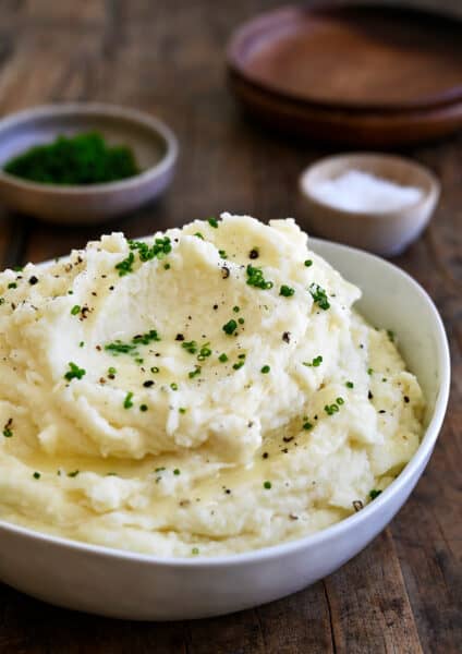 Creamy mashed potatoes topped with fresh chives and black pepper in a white serving bowl.