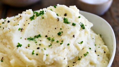 Creamy mashed potatoes topped with fresh chives and black pepper in a white serving bowl.