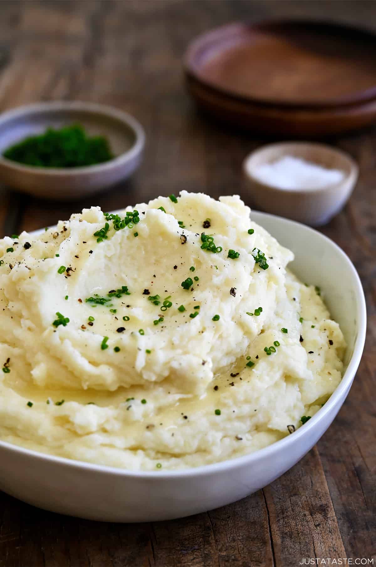 Creamy mashed potatoes topped with fresh chives and black pepper in a white serving bowl.