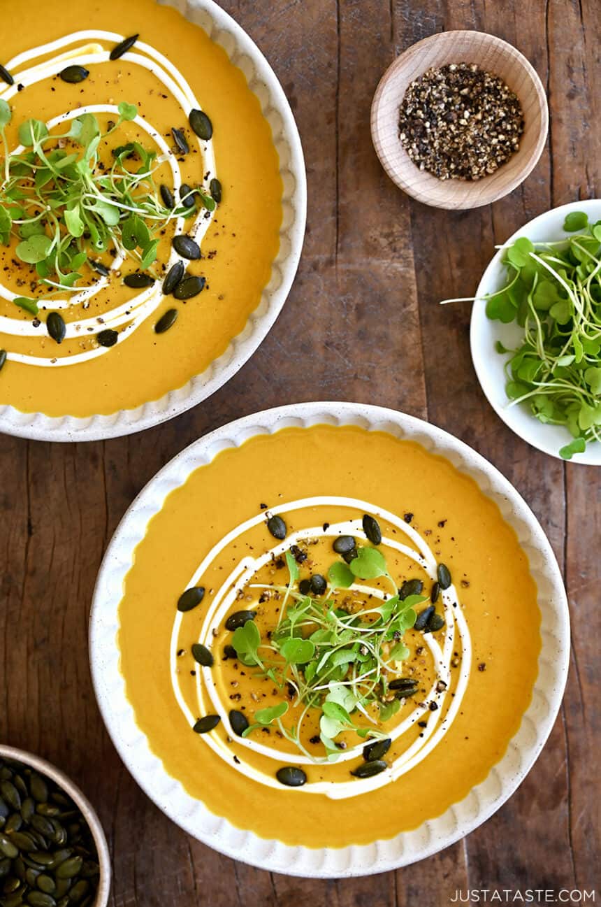 A top-down view of two bowls containing the best Thai Coconut Pumpkin Soup topped with toasted pumpkin seeds, micro greens and a drizzle of sour cream