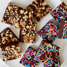 Homemade microwave fudge topped with rainbow sprinkles and chopped walnuts on a white plate.