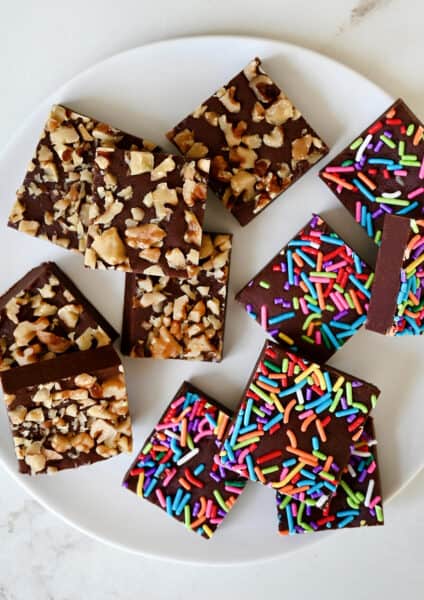Homemade microwave fudge topped with rainbow sprinkles and chopped walnuts on a white plate.