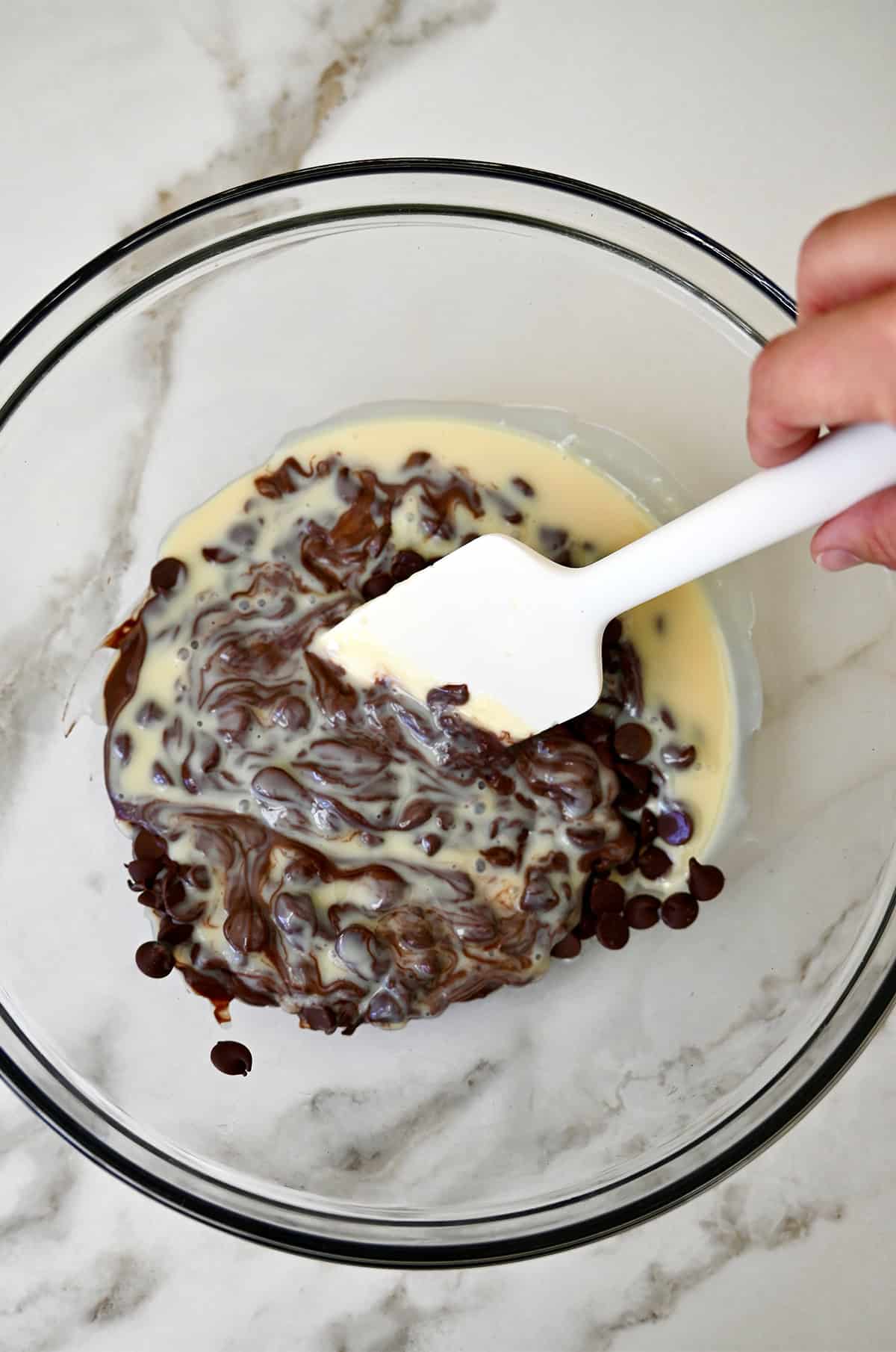 Mixing semi-melted chocolate chips with condensed milk in a bowl.