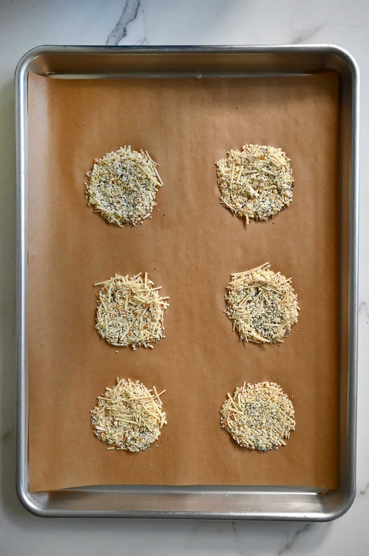 Circles of Parmesan cheese on a parchment paper-lined baking sheet before baking into cheese crisps.