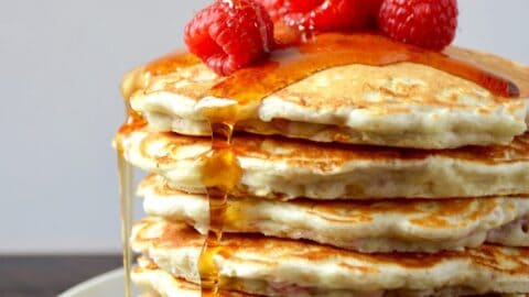 Tall stack of Raspberry Oatmeal Pancakes topped with fresh raspberries and maple syrup