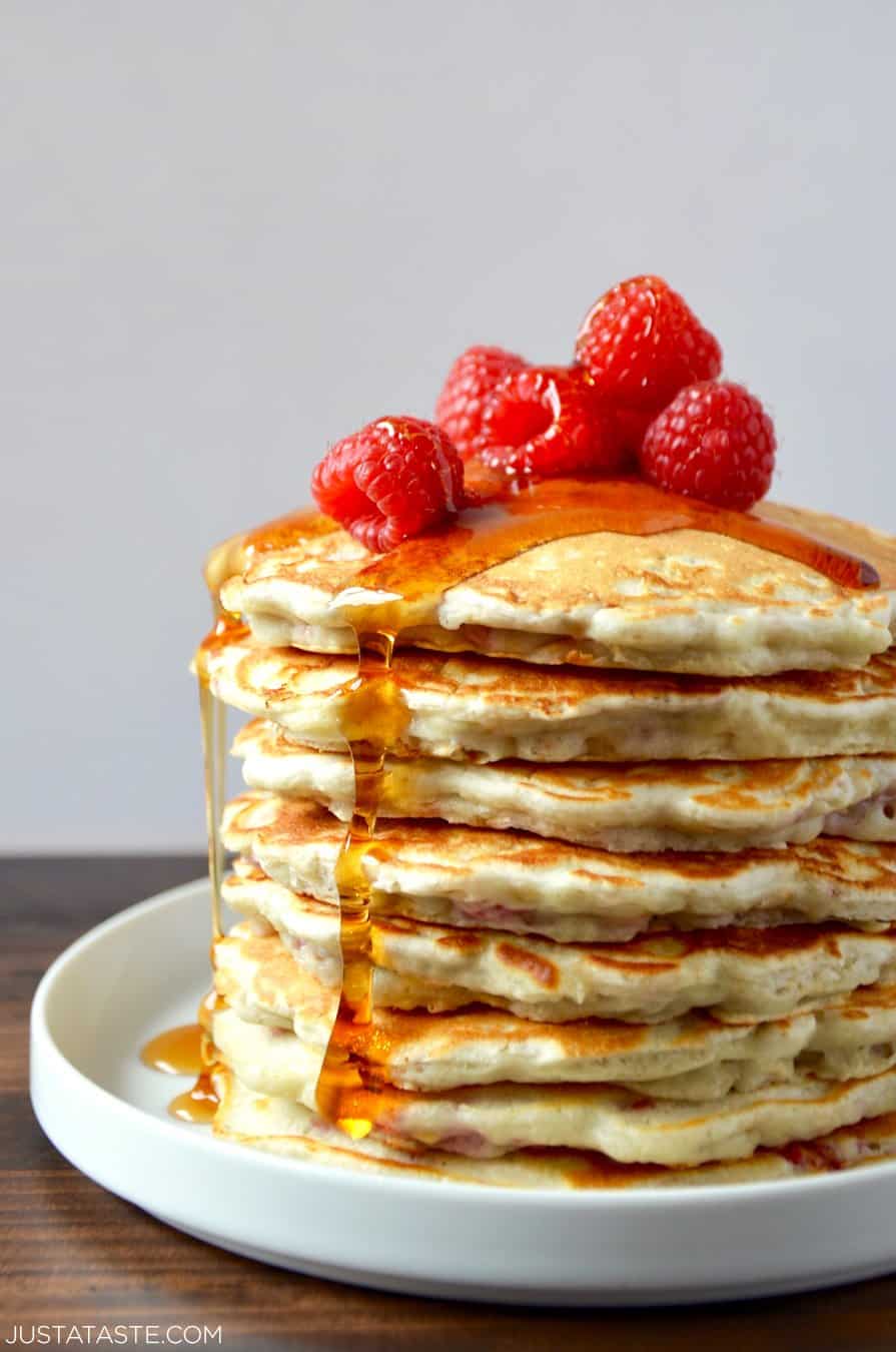 Tall stack of Raspberry Oatmeal Pancakes topped with fresh raspberries and maple syrup