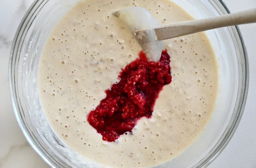 Mashed berries being stirred into batter with a spatula 