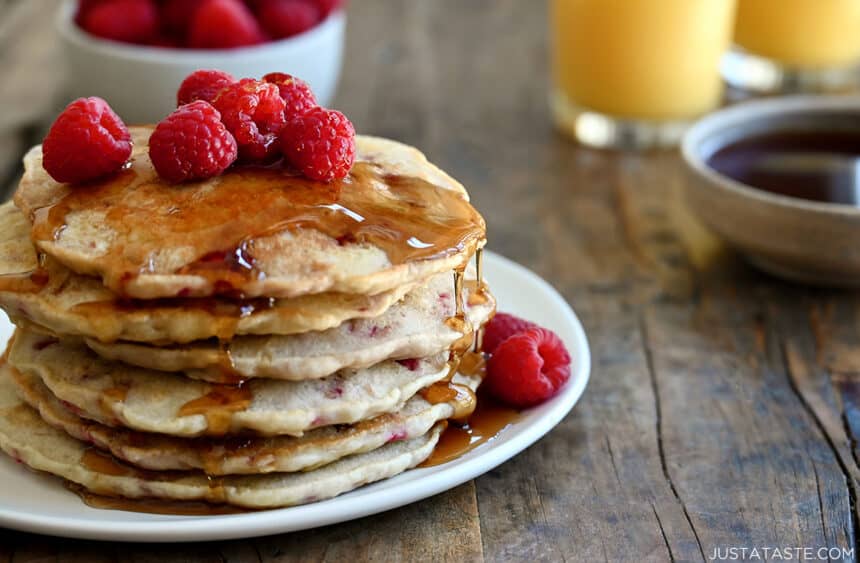 A tall stack of Raspberry Oatmeal Pancakes topped with fresh raspberries and drizzled with maple syrup