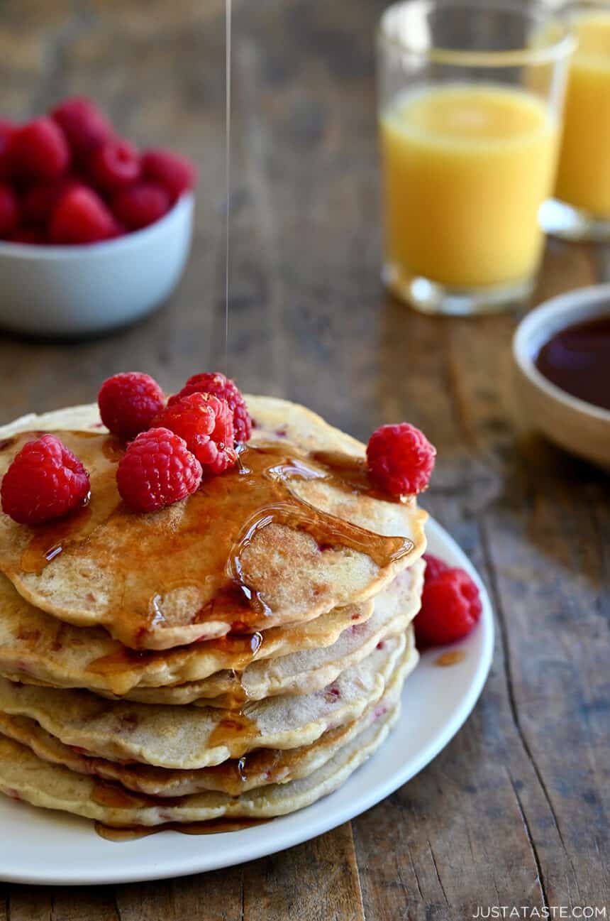 A tall stack of Raspberry Oatmeal Pancakes topped with maple syrup and fresh raspberries