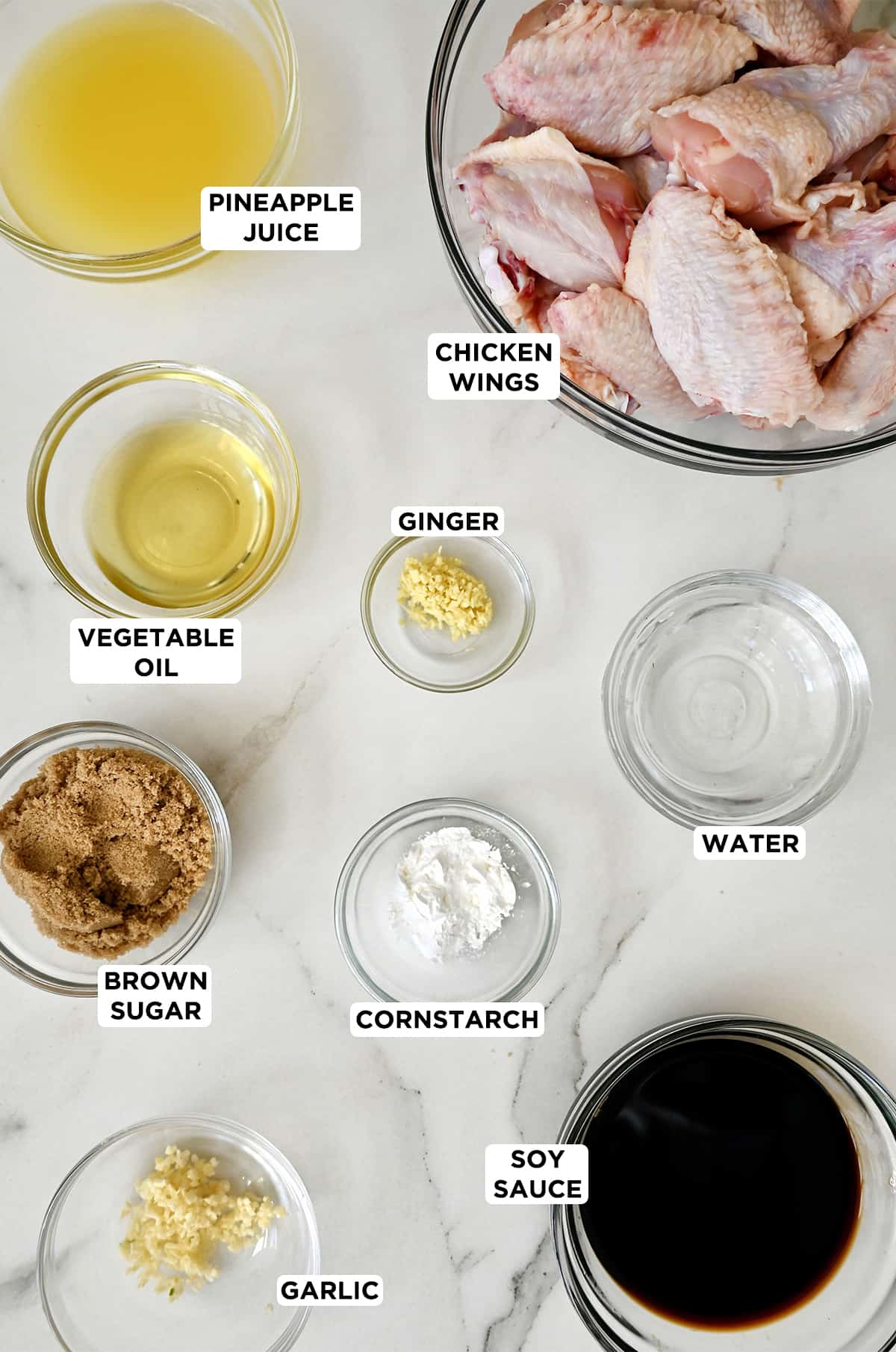 Various sizes of glass bowls containing chicken wings, water, minced ginger, cornstarch, soy sauce, brown sugar, vegetable oil, minced garlic and pineapple juice.