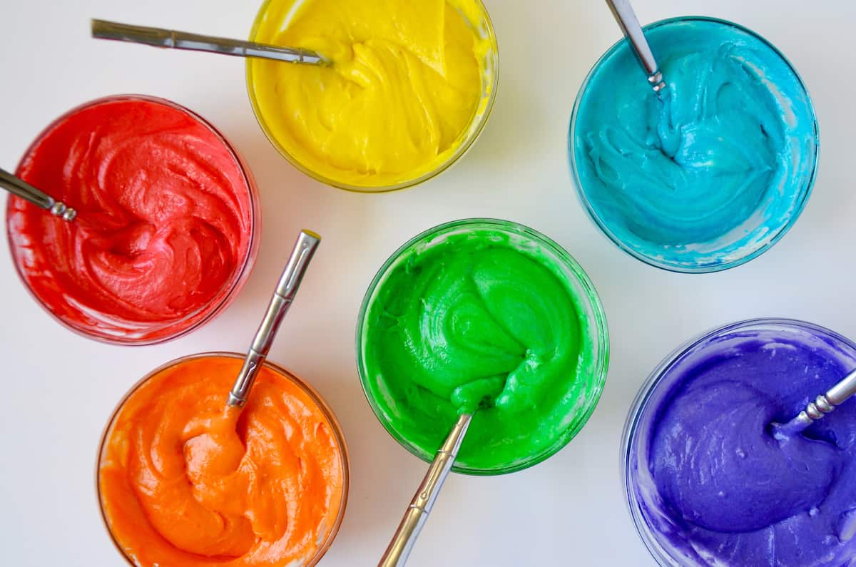 Small bowls are filled with cupcake batter tinted every color of the rainbow. A spoon is in each bowl.