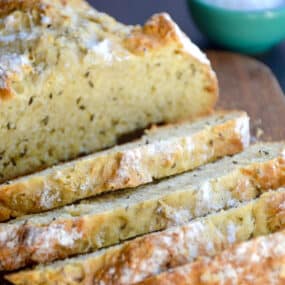 Half a loaf of homemade soda bread with caraway seeds sliced on a cutting board.