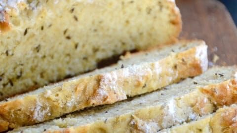 Half a loaf of homemade soda bread with caraway seeds sliced on a cutting board.