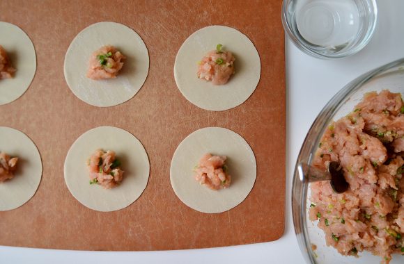 Ground chicken mixture atop wonton wrappers on wood cutting board