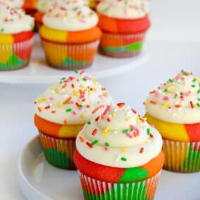 Rainbow Cupcakes with Buttercream Frosting and sprinkles on white plate.