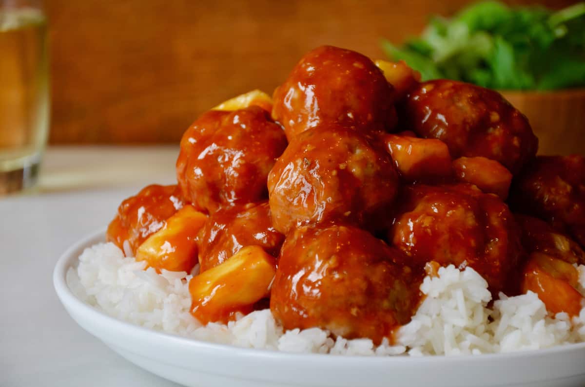 Sweet and sour meatballs with pineapple chunks atop rice in a dinner bowl.