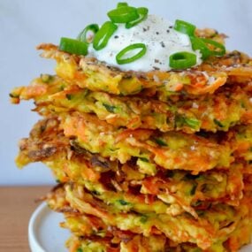 Stack of Quick and Crispy Vegetable Fritters topped with sour cream and sliced scallions
