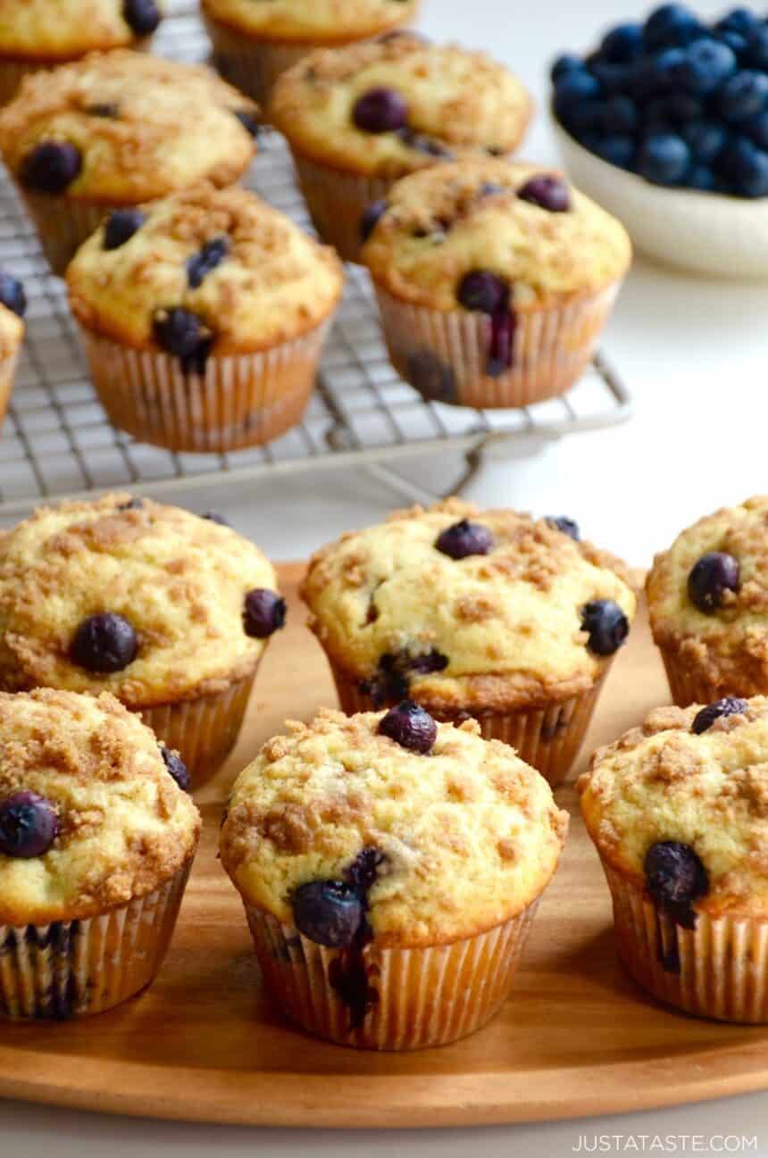 Blueberry Coffee Cake Muffins with Streusel on a serving plate with more muffins on a wire cooling rack in the background