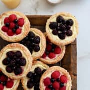 A top-down view of Fruit and Cream Cheese Breakfast Pastries on a wood serving platter next to glasses filled with orange juice and a bowl with fresh raspberries