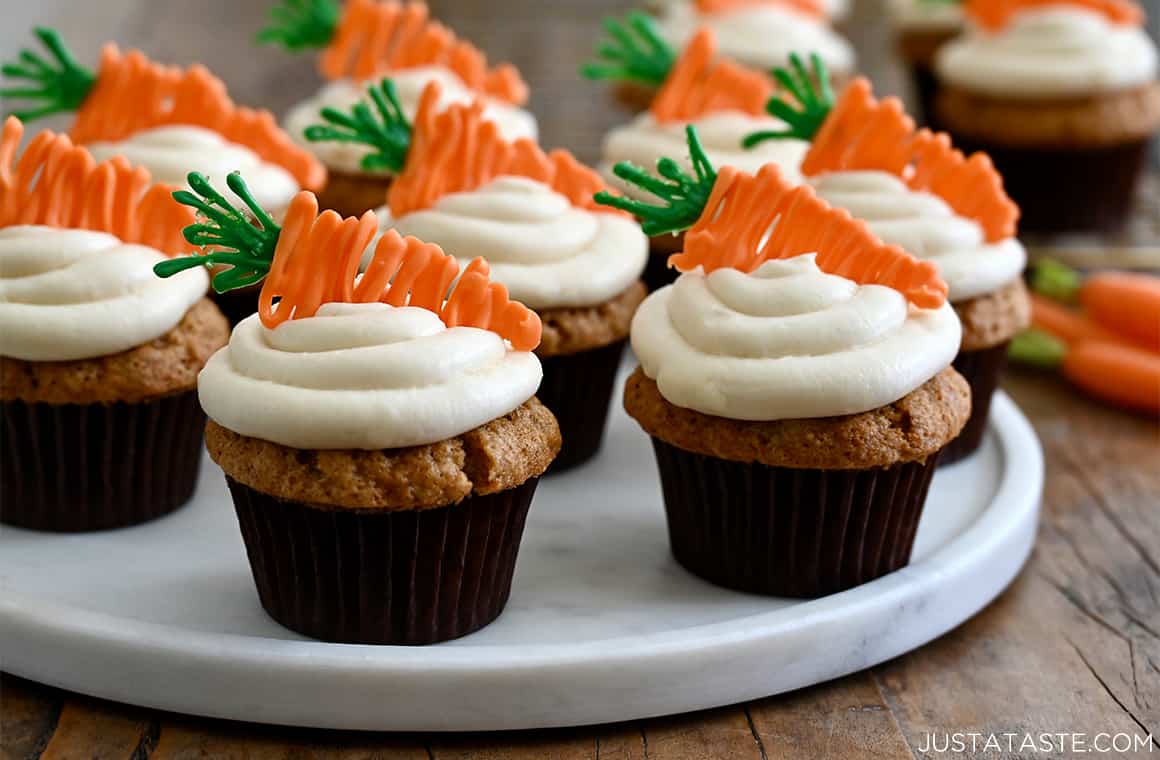 A close-up view of cupcakes with swirled frosting and candy melt toppers on a marble serving platter.