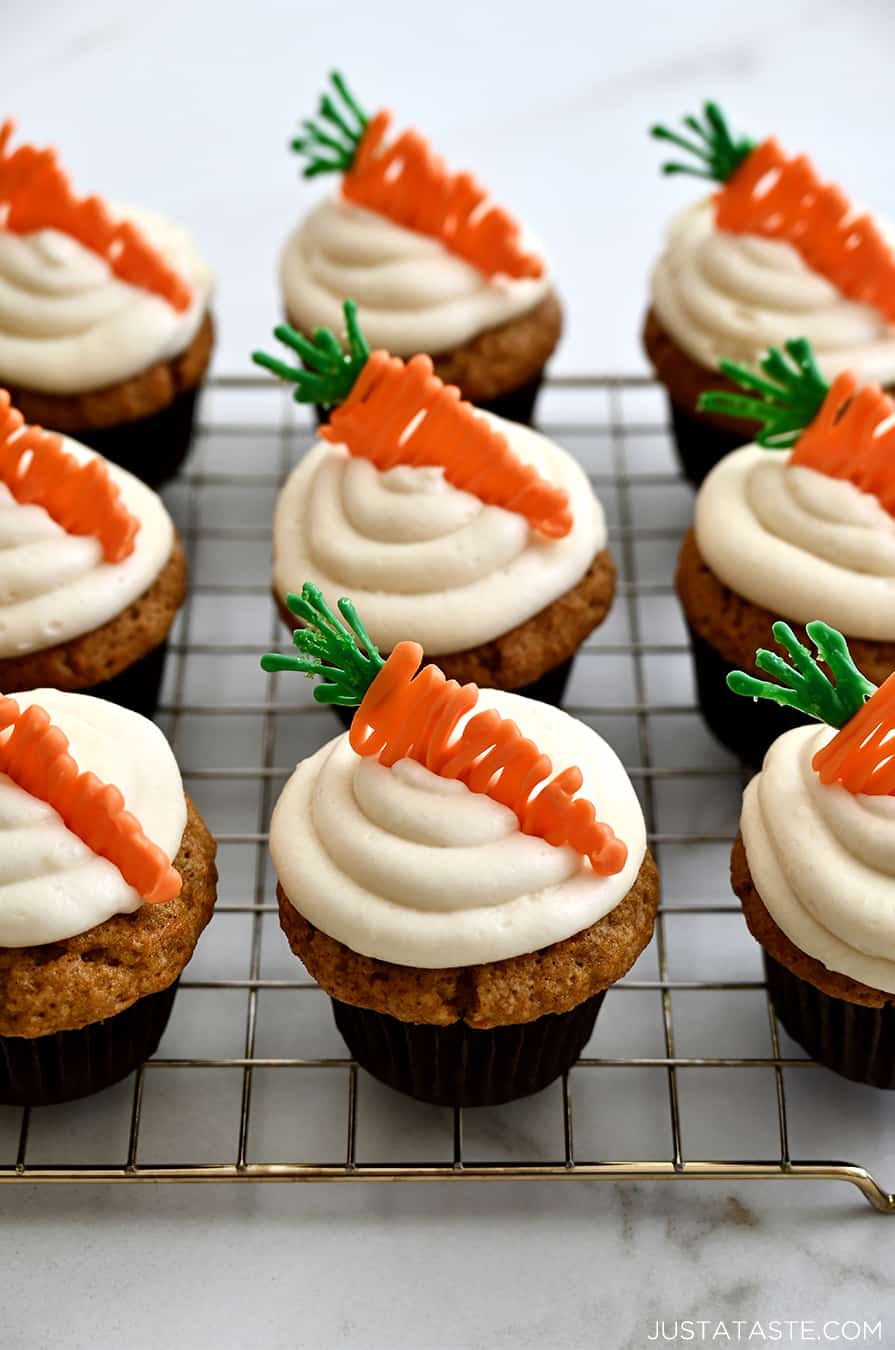 Carrot cake cupcakes with swirled cream cheese frosting and candy melt toppers on a cooling rack.