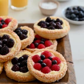 Fruit and Cream Cheese Breakfast Pastries on a wood serving platter next to two glasses of orange juice