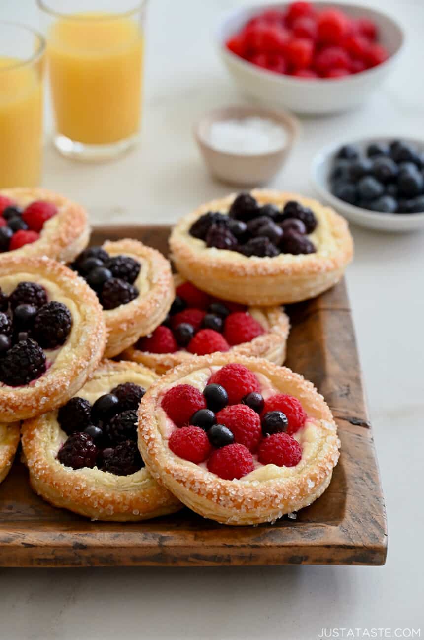 Fruit and Cream Cheese Breakfast Pastries on a wood serving platter next to two glasses of orange juice