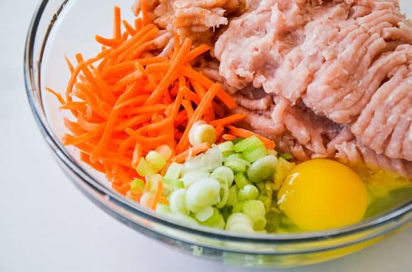 A glass bowl containing ground chicken, carrots, scallions and egg