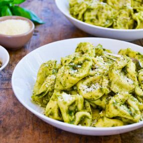 Two bowls filled with Pistachio Pesto Tortellini with fresh basil in the background