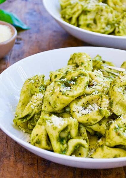 Two bowls filled with Pistachio Pesto Tortellini with fresh basil in the background