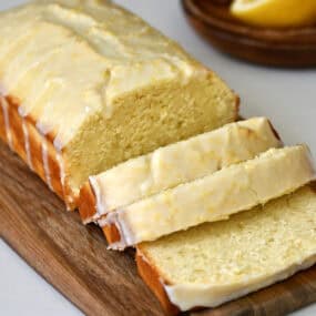 Glazed lemon loaf slices on a small wood cutting board.
