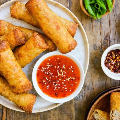 A white plate containing chicken egg rolls and a small bowl of sweet-and-sour sauce