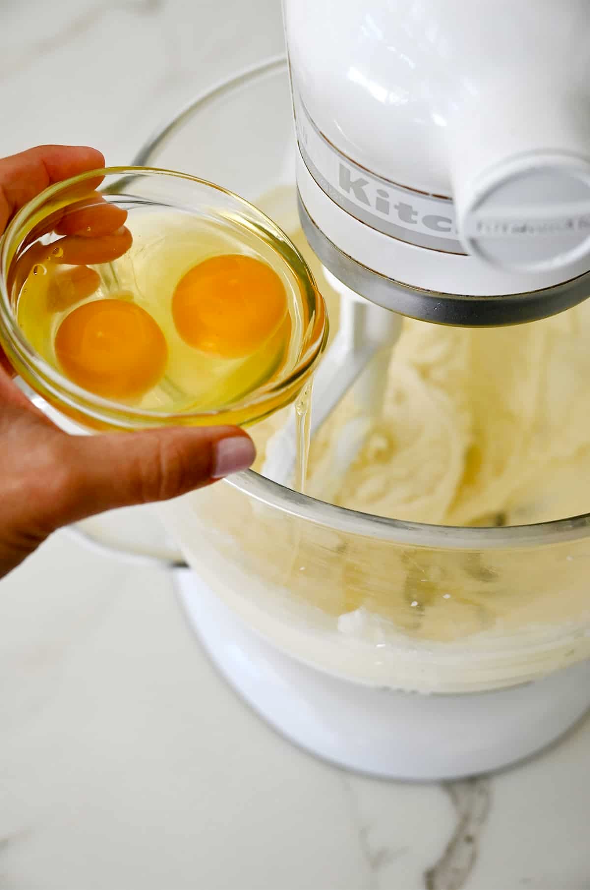 Adding eggs to a stand mixer bowl with creamed butter and sugar.