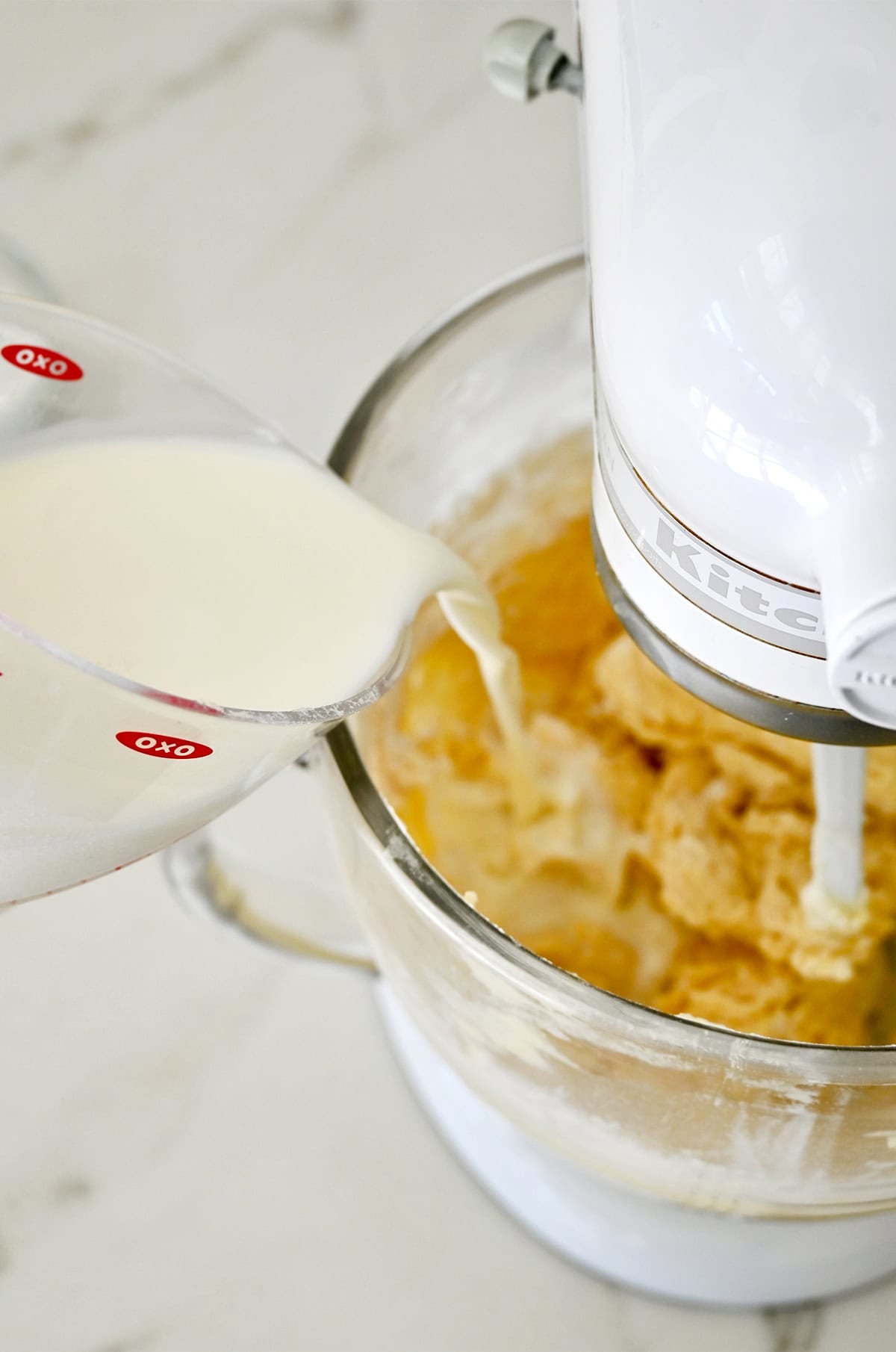 Adding milk to a stand mixer bowl to make a rich vanilla cupcake batter.