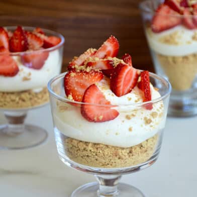 Easy No-Bake Cheesecake Parfaits in individual glasses topped with sliced fresh strawberries and graham cracker crumbles