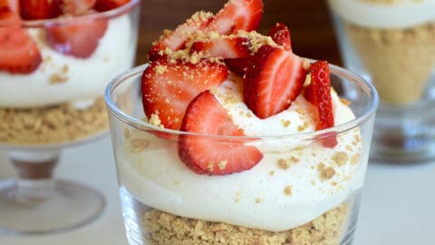 Easy No-Bake Cheesecake Parfaits in individual glasses topped with sliced fresh strawberries and graham cracker crumbles