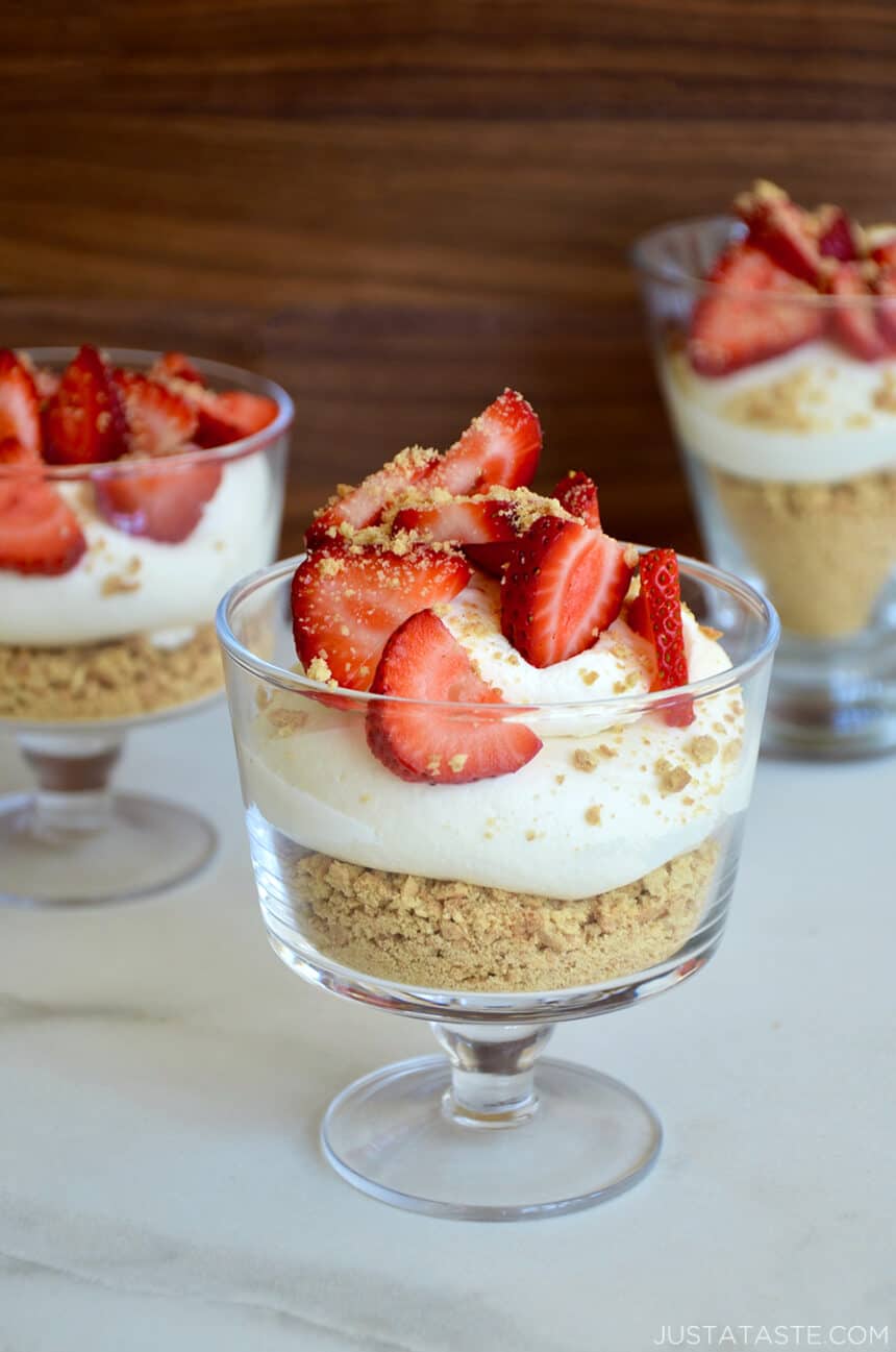 Easy No-Bake Cheesecake Parfaits in individual glasses topped with sliced fresh strawberries and graham cracker crumbles