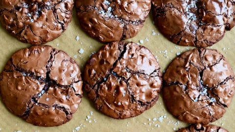 A child's hand reaches for a flourless cookie with chocolate chips topped with large-flake sea salt