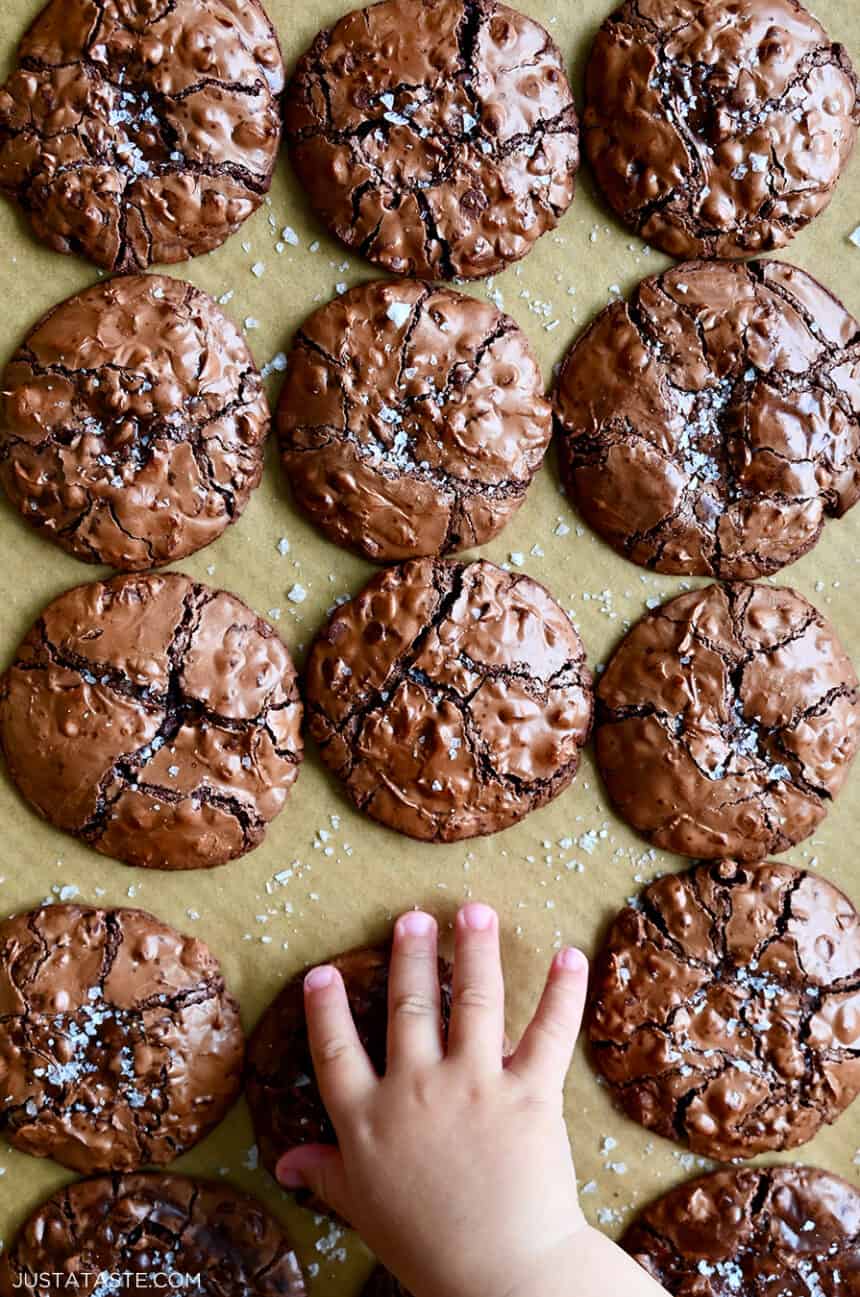 A child's hand reaches for a flourless cookie with chocolate chips topped with large-flake sea salt